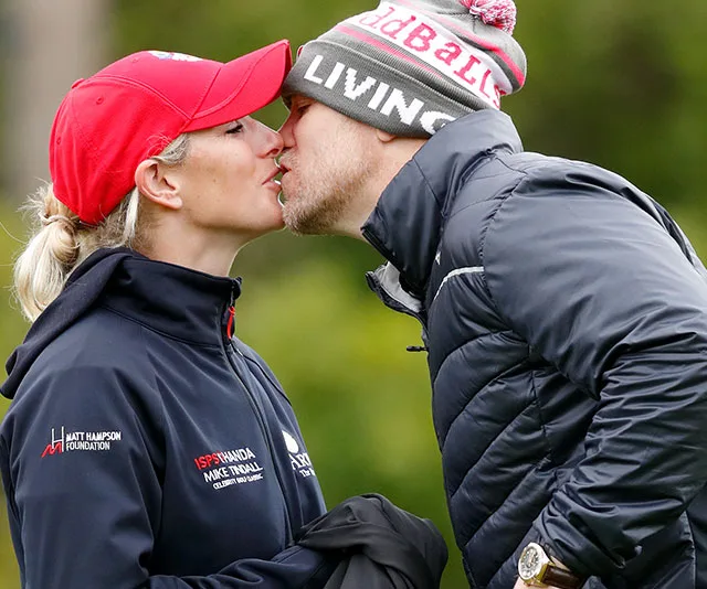 A couple shares a kiss outdoors, both wearing hats and jackets, in a natural setting.