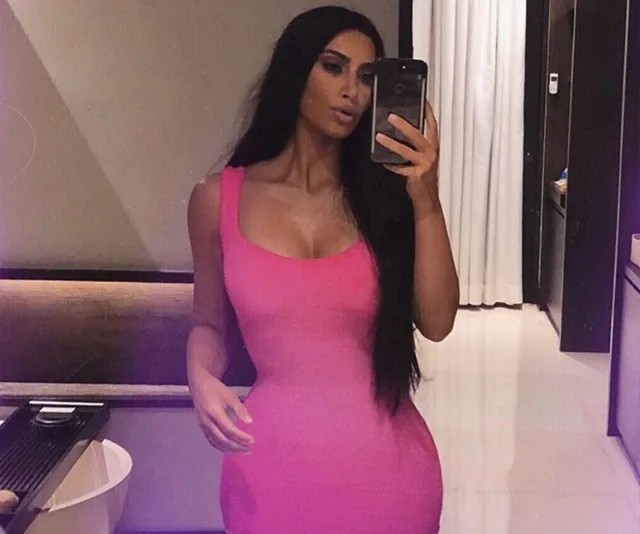 A woman taking a mirror selfie in a pink dress.