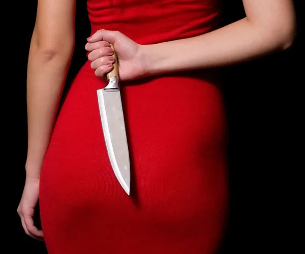 A woman in a red dress holds a large kitchen knife behind her back.