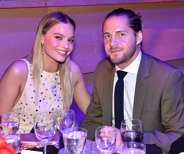 Two people smiling at a dining table with glasses, plates, and centerpieces in a softly lit room.