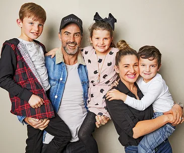 A happy family of five poses together; parents each holding a child, with another child smiling in the middle.