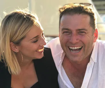 A man and woman smiling together outdoors, with a bright, sunny background.