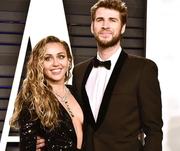 A couple poses together at a formal event, with one wearing a black sequined dress and the other in a black tuxedo.