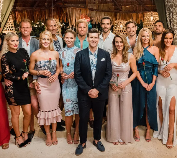 Group photo of "Bachelor in Paradise" contestants holding roses, standing together in a tropical setting.