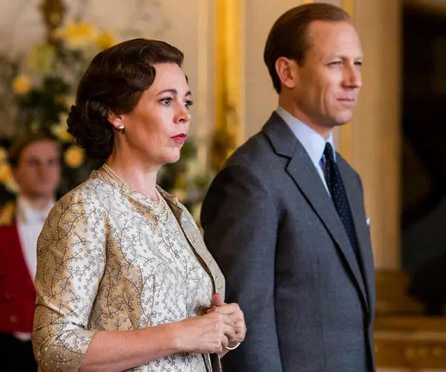 Two characters from "The Crown" season 3 stand in a formal setting, both wearing elegant attire.