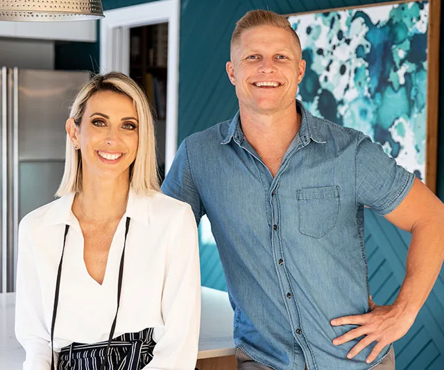 Man and woman smiling in a modern kitchen with teal and white decor.