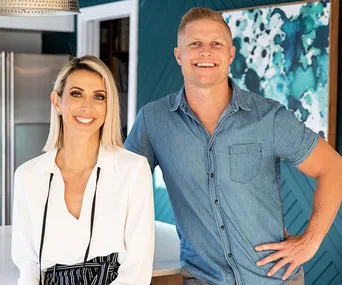 Man and woman smiling in a modern kitchen with teal and white decor.