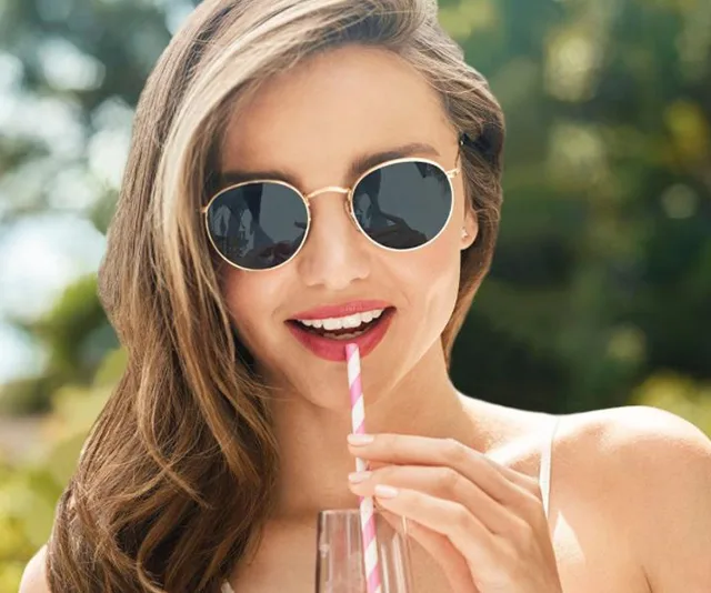 Woman in sunglasses drinking through a striped straw outdoors.