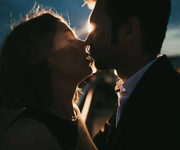 A couple in silhouette, sharing an intimate moment against a dimly lit background.