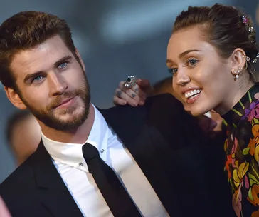 A woman smiling and leaning towards a man in a suit, both posing at an event.
