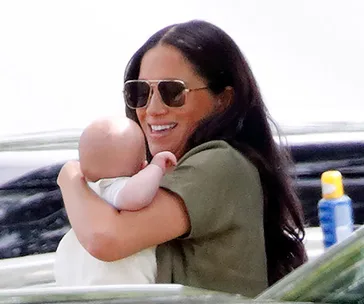 Woman in sunglasses smiling while holding a baby outdoors.