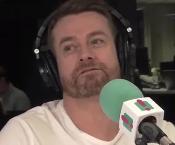 Radio host wearing headphones speaks into a studio microphone.