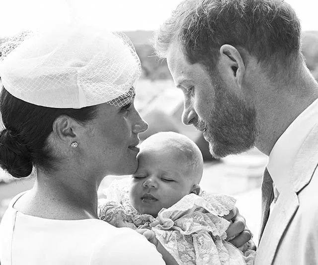 A couple lovingly gazes at their baby, who is peacefully asleep in their arms, in a serene outdoor setting.