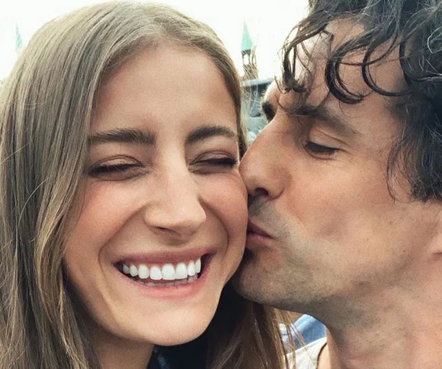 A happy couple is posing for a selfie; one person is kissing the other's cheek while both are smiling broadly.