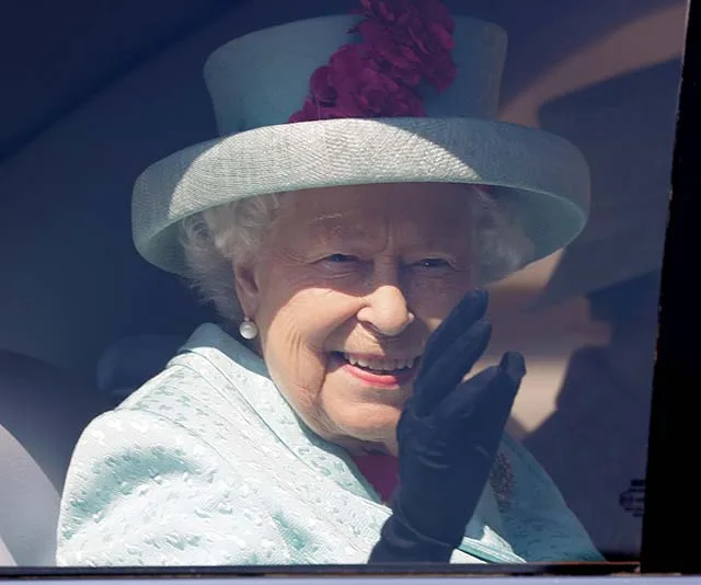 Elderly woman in a hat waving from a car window, smiling warmly.