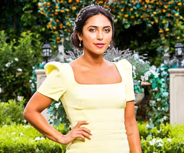 Woman in a yellow dress with a decorative hairpiece standing in a lush garden setting.