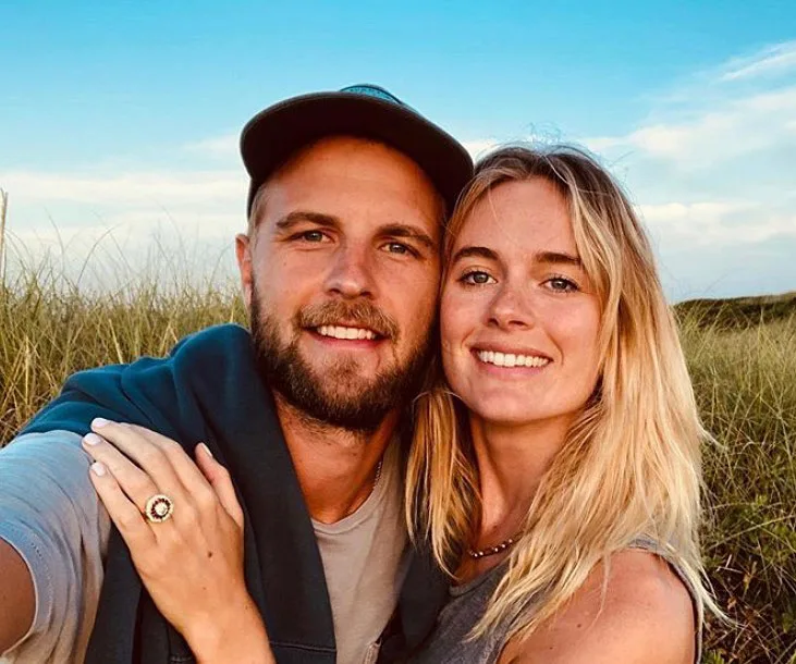 Couple smiling and posing outdoors, with the woman wearing an engagement ring.