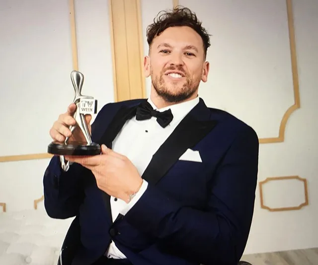 Man in a suit holding an award, smiling at the camera.