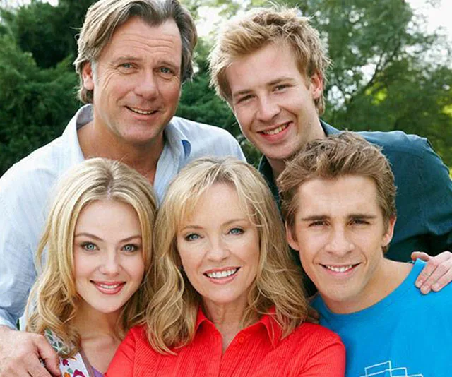 Group photo of smiling cast members from "Packed to the Rafters," outdoors with trees in the background.