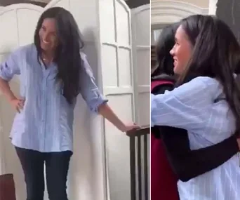 Woman in a striped shirt smiling and hugging someone indoors.