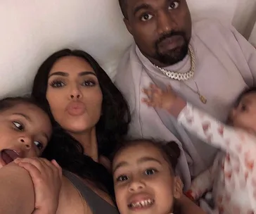 Family selfie with a woman, a man, and four young kids smiling and cuddling together.