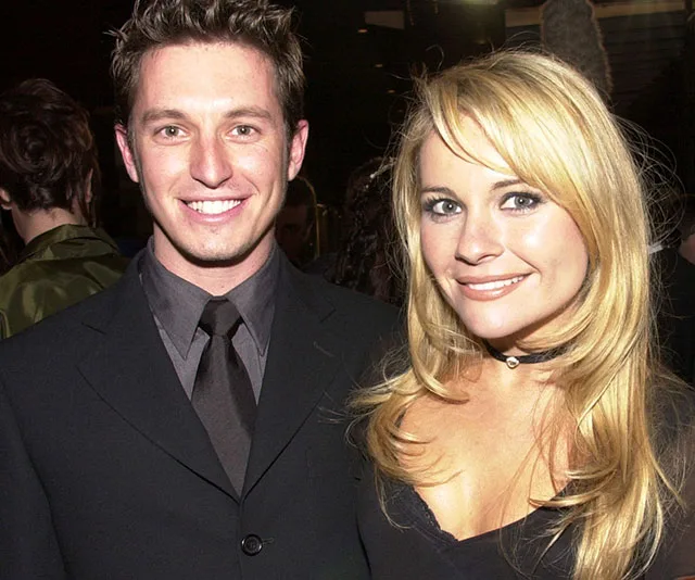 A smiling couple dressed in formal attire at a public event, with the woman wearing a choker necklace.