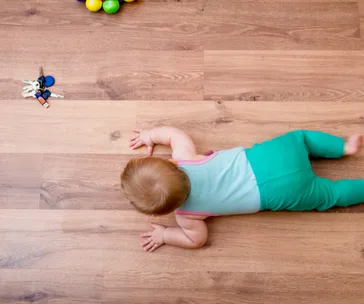 Baby crawling on wooden floor towards a set of keys, wearing a turquoise and pink outfit.