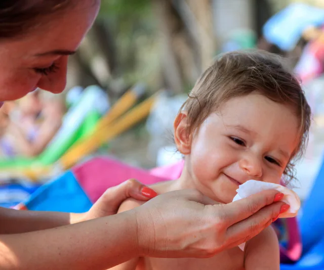 A baby being gently wiped by an adult with a soft cloth, smiling outdoors in a colorful setting.