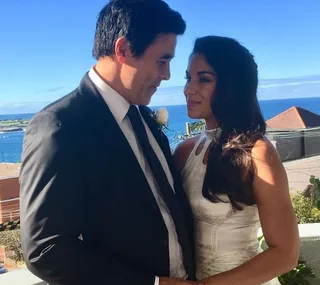 A couple in wedding attire share a loving gaze on a sunny day by the ocean.
