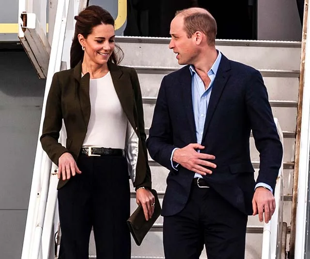Two people in business attire walking down airplane stairs, smiling and conversing.