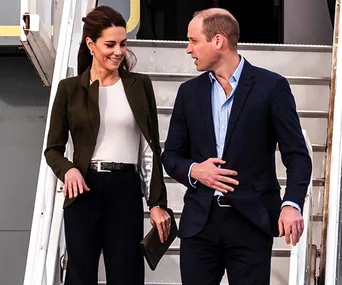 Two people in business attire walking down airplane stairs, smiling and conversing.