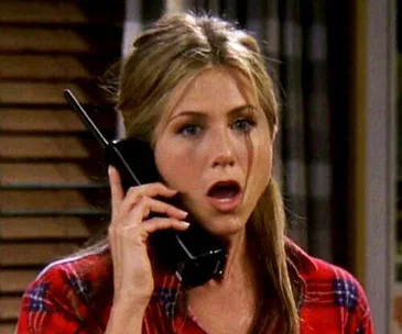 Rachel Green from "Friends" on a phone call, looking surprised, wearing a red plaid shirt.