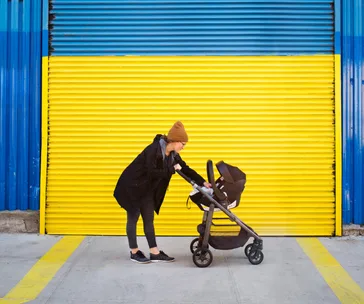 Person in a beanie pushes a stroller in front of a yellow and blue garage door.