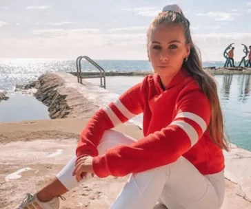 Woman in red sweater sitting by a seaside pool, under a clear sky.