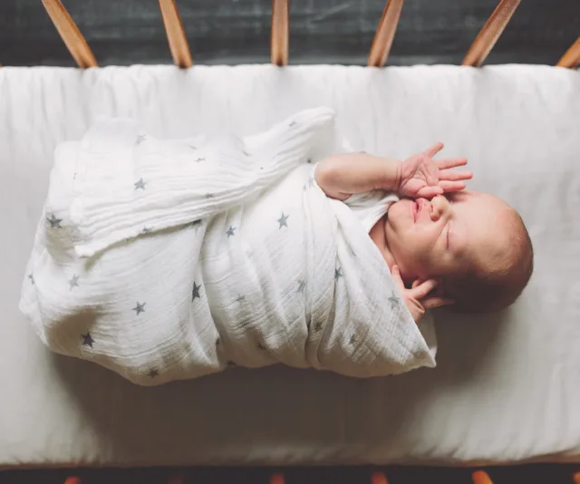 Newborn baby swaddled in a white blanket with star patterns, lying in a crib.