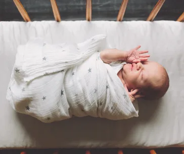 Newborn baby swaddled in a white blanket with star patterns, lying in a crib.