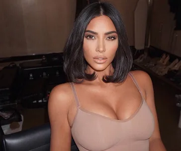 Alt text: "Person with dark hair wearing a nude-colored tank top seated indoors."