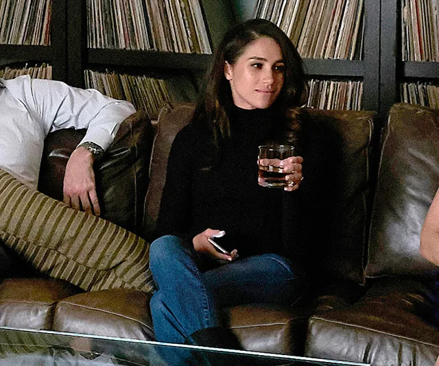 A person sitting on a couch holding a drink, with vinyl records in the background.