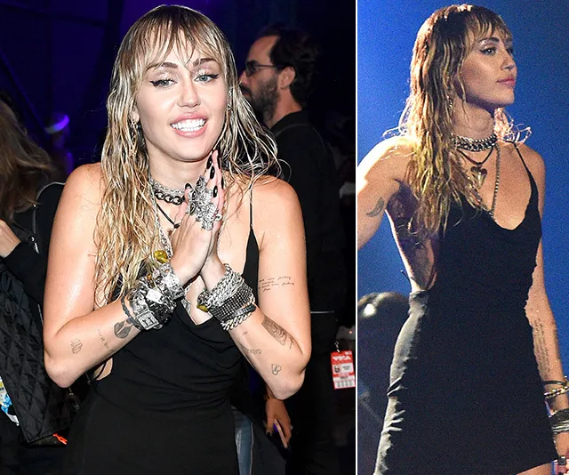 Miley Cyrus at VMAs 2019, wearing a black dress and layered jewelry, smiling and performing on stage.