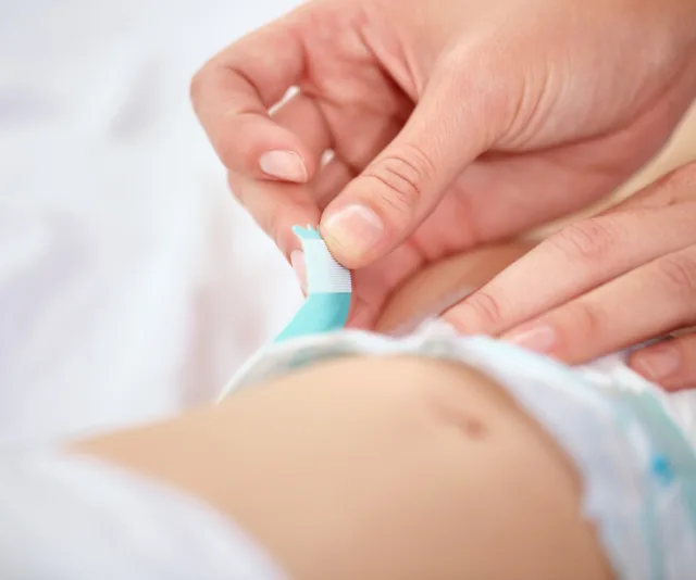 Baby's diaper being adjusted by an adult's hands.
