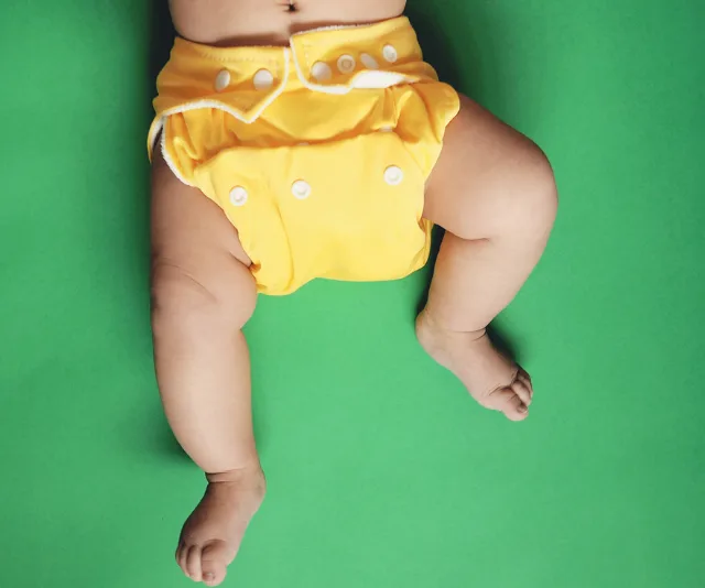 Baby wearing a bright yellow reusable nappy on a green background.