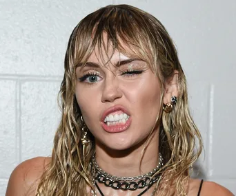 Singer with wet hair winking, showcasing chain necklaces and bold earrings in a playful expression.