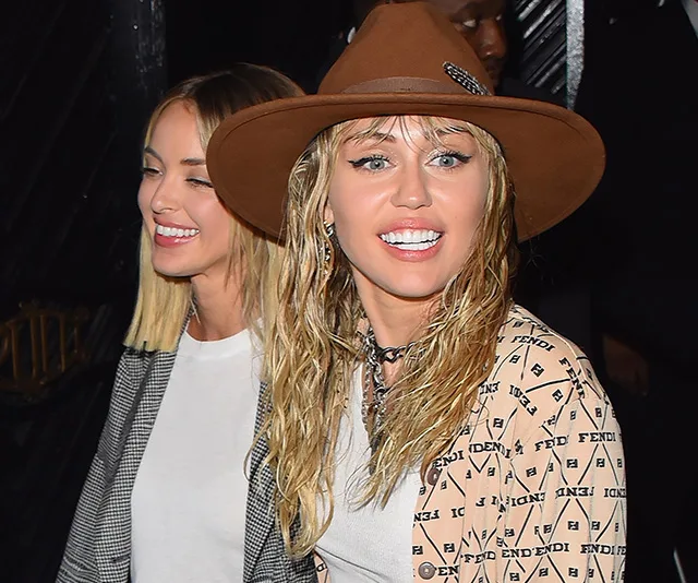 Two women smiling, one with a hat and wet hair, in casual outfits at an event.