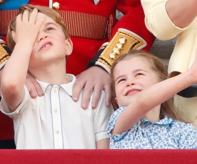 Two children smiling and looking upwards with an adult behind them in ceremonial attire.