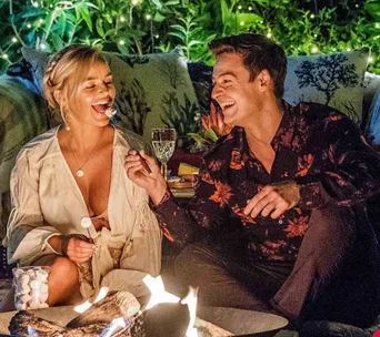 A couple roasting marshmallows by a fire, smiling and enjoying a cozy evening outside.