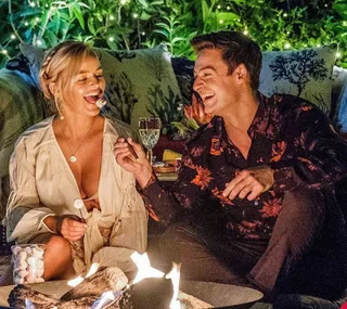 A couple roasting marshmallows by a fire, smiling and enjoying a cozy evening outside.