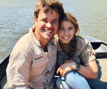 Couple smiling on a boat by the water, wearing matching shirts with names "Chandler" and "Bindi."