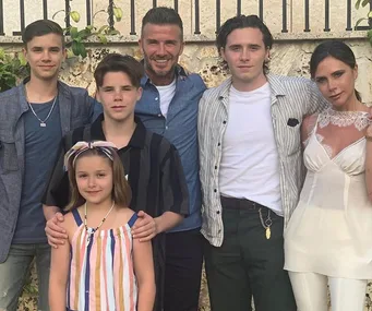Family of six posing together, standing outside by a stone wall; three adults and three children.