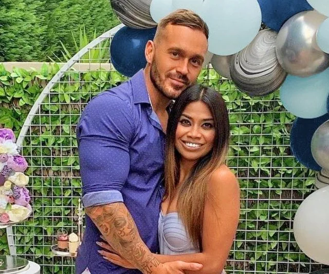 A couple posing outdoors at an event with a balloon backdrop, smiling together.