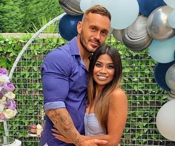 A couple posing outdoors at an event with a balloon backdrop, smiling together.